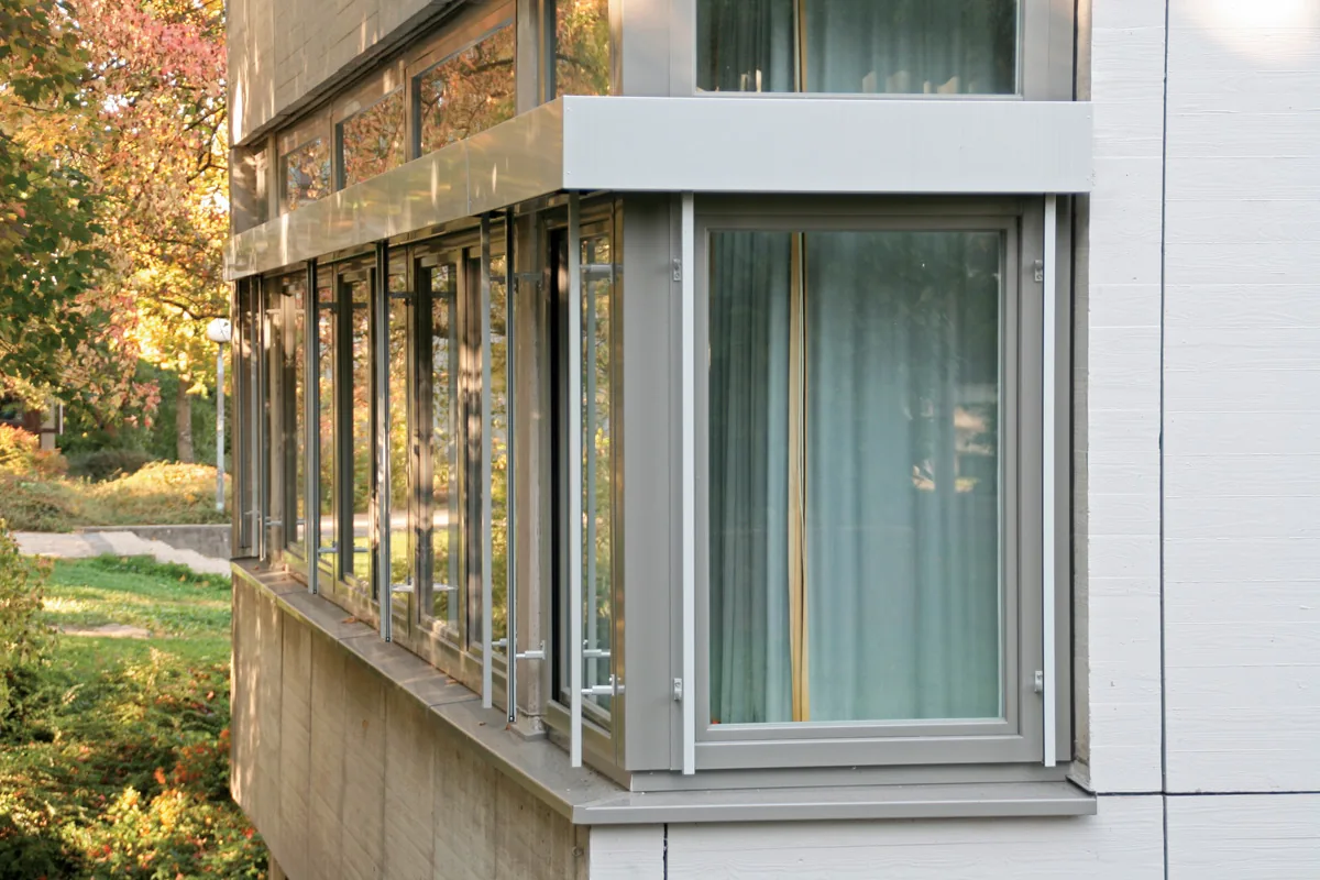 Ventana de madera-aluminio con hoja corredera y carpintería gris junto a un jardín
