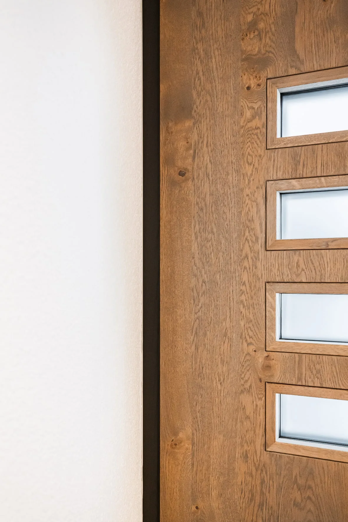 Detalle de puerta de entrada de roble con vidrios horizontales junto a un marco oscuro